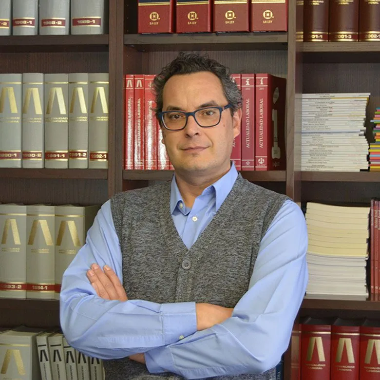 Juan Antonio Barceló, con gafas y los brazos cruzados, delante de una estantería de libros